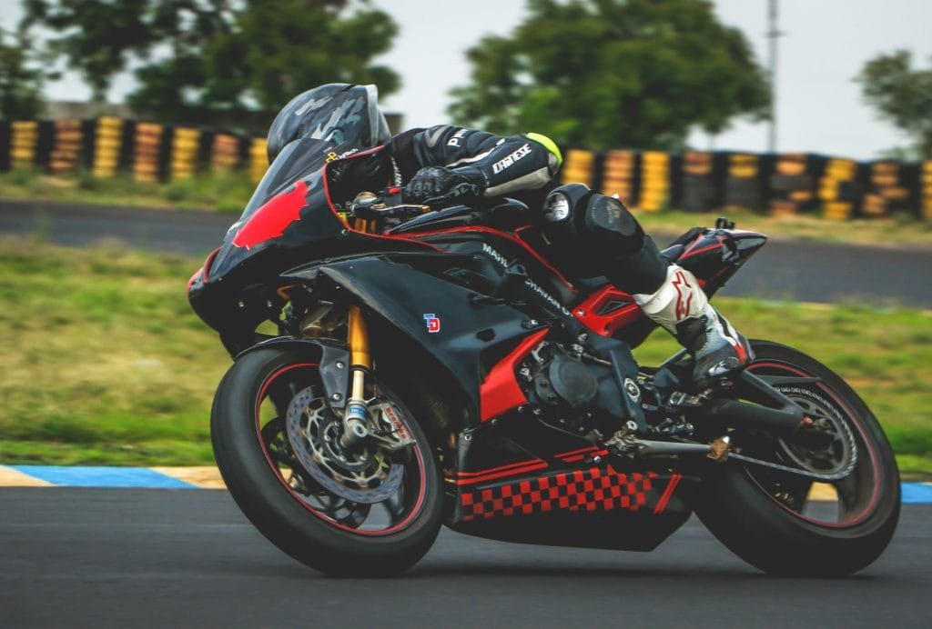 man with black alpinestar racing suit riding black and red sports bike